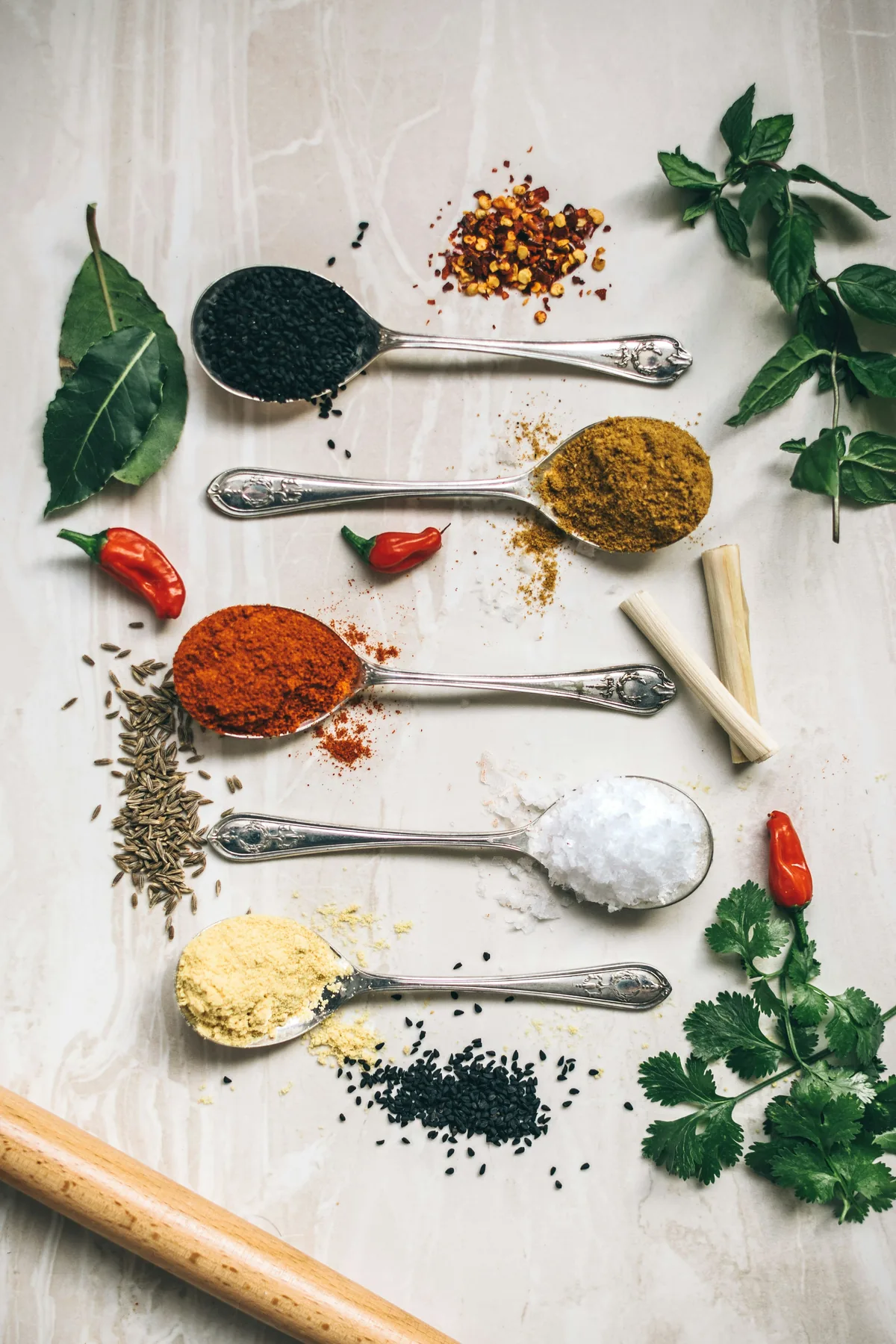 Assorted ground and whole Indian spices arranged on silver spoons